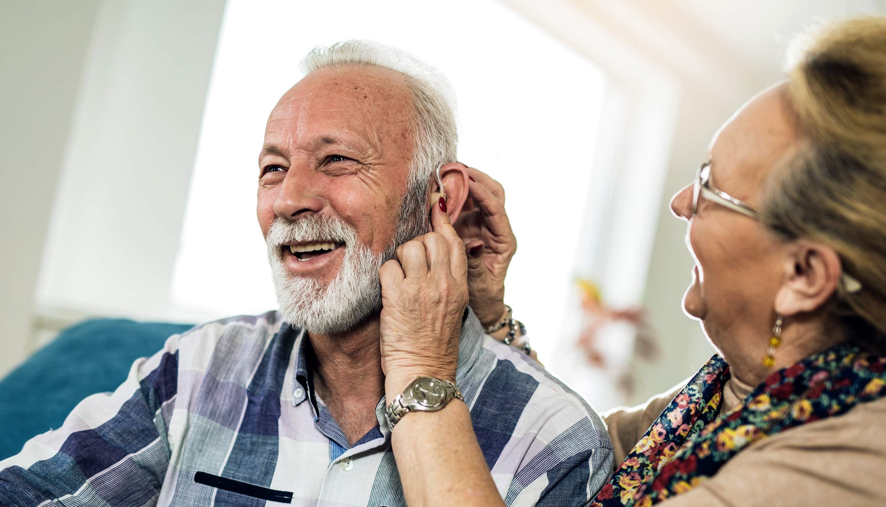 2 older adults (man and woman) helping each other put on a medical devices device in their ears to hear better, happy to be able to help themselves