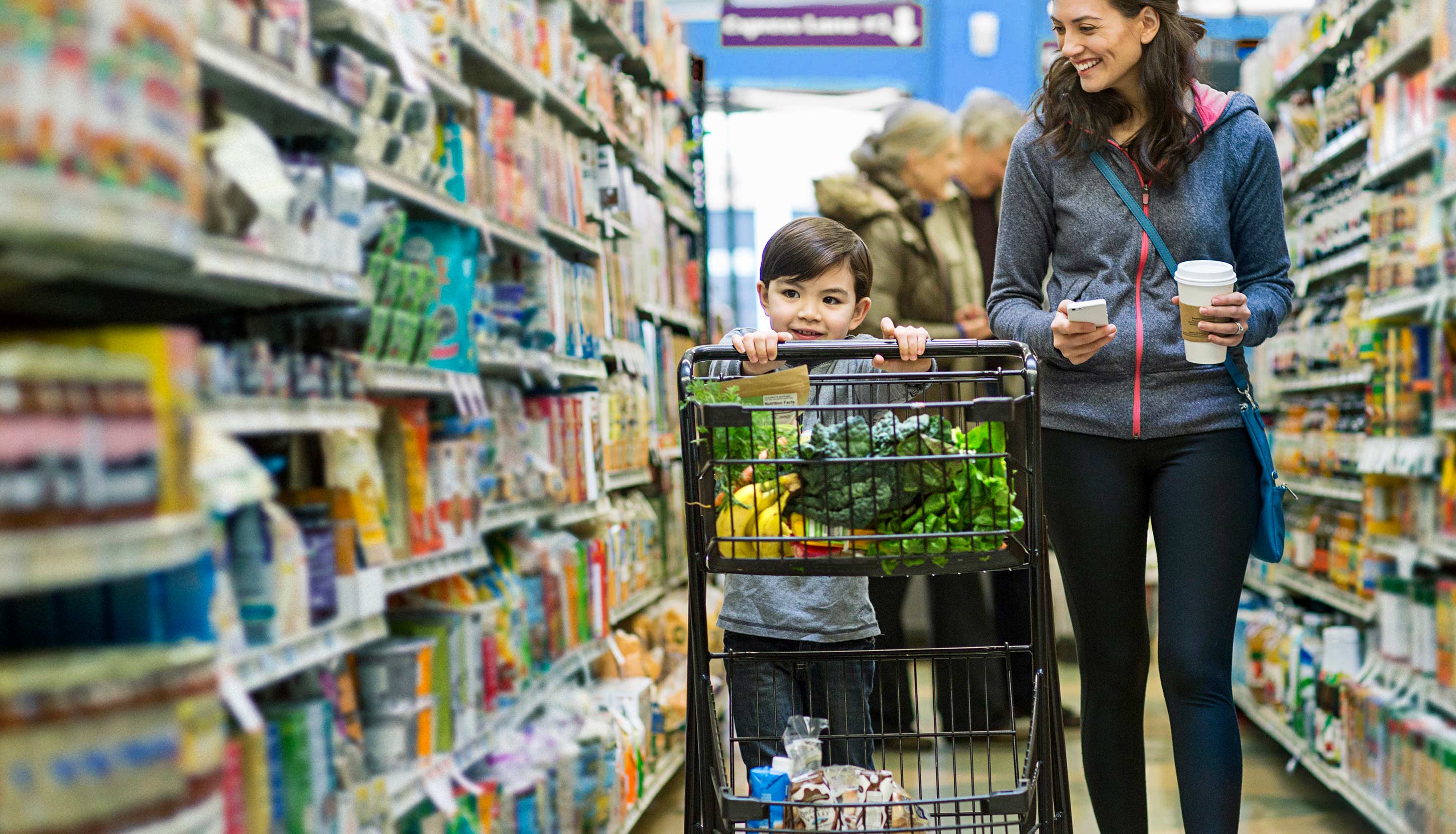 A woman with a child walking through a supermarket having vegetables in the shopping cart