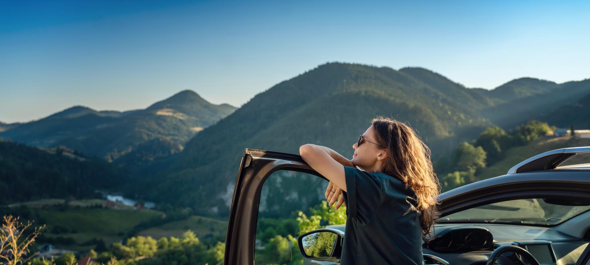 Young woman traveling by car in the mountains, looking into nature.