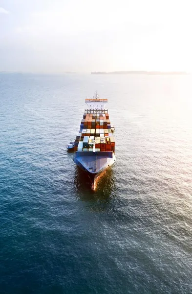 Aerial view of a container vessel front with sun and harbour in the back